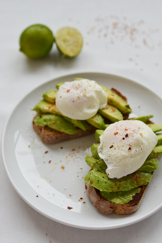 Sliced avocado on toasted bread with a poached egg on top, sprinkled with seasonings on a white plate with a white background.