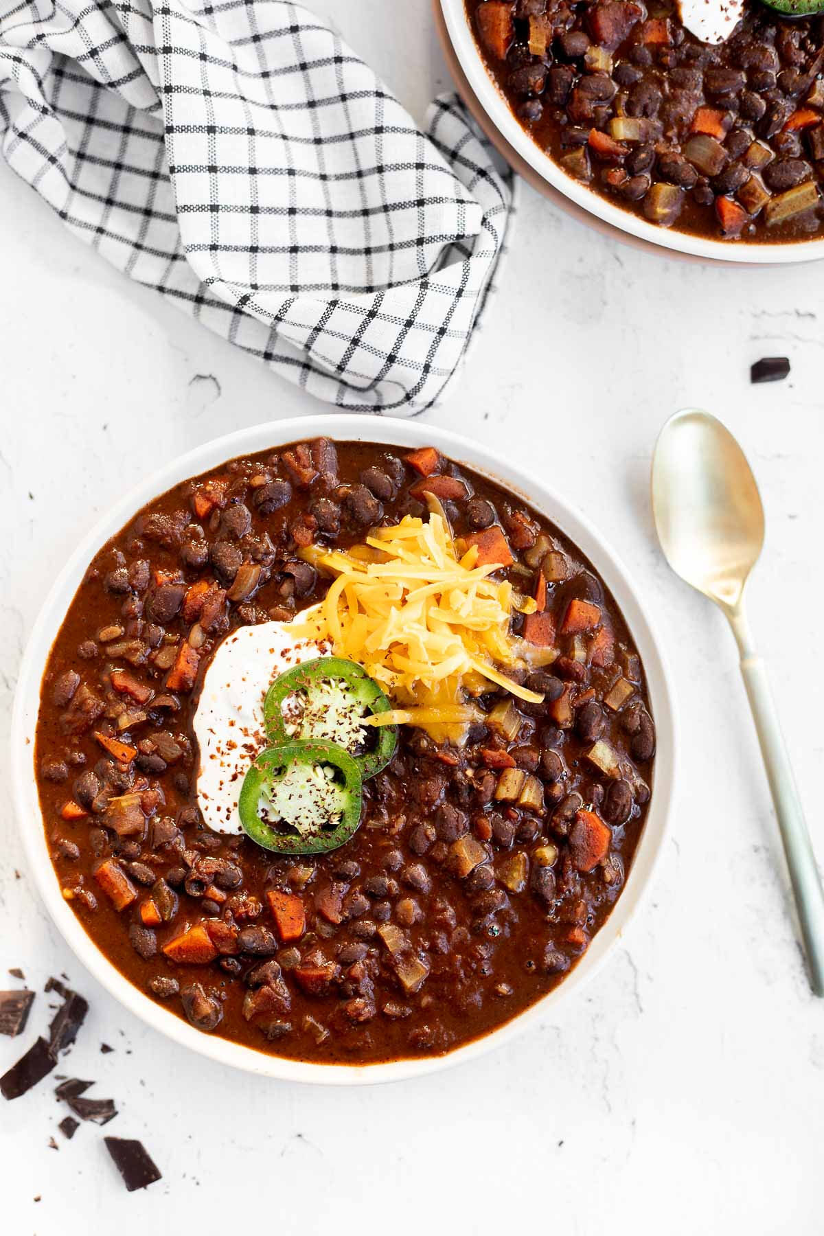 Black Bean Chili with Chocolate in a white bowl garnished with jalapeno slices, sour cream, and shredded cheddar, top view.
