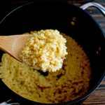 Cooked quinoa in a wooden spoon over a saucepan.