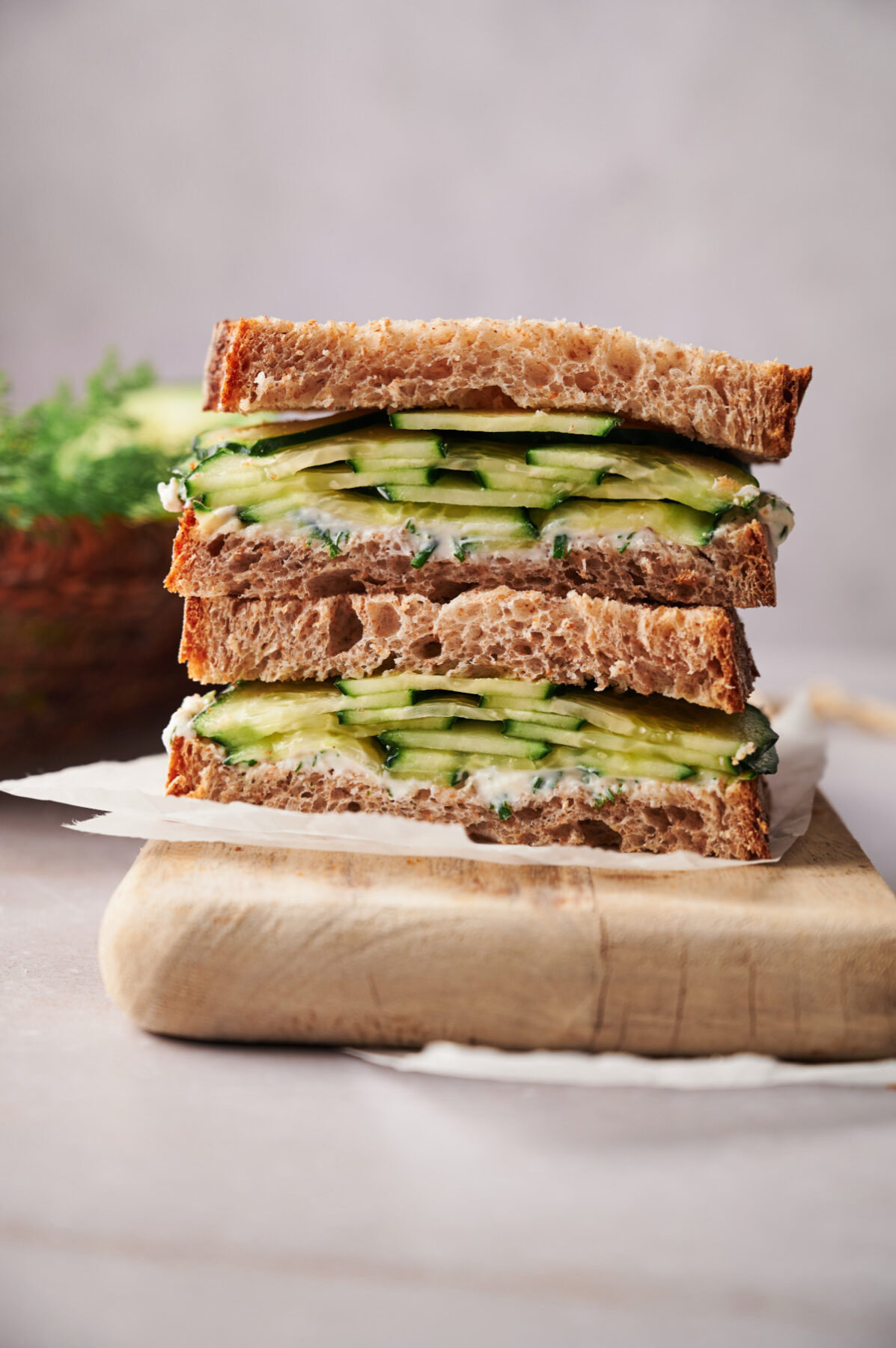 Vertical image of a cucumber sandwich sliced in half and stacked on a cutting board.