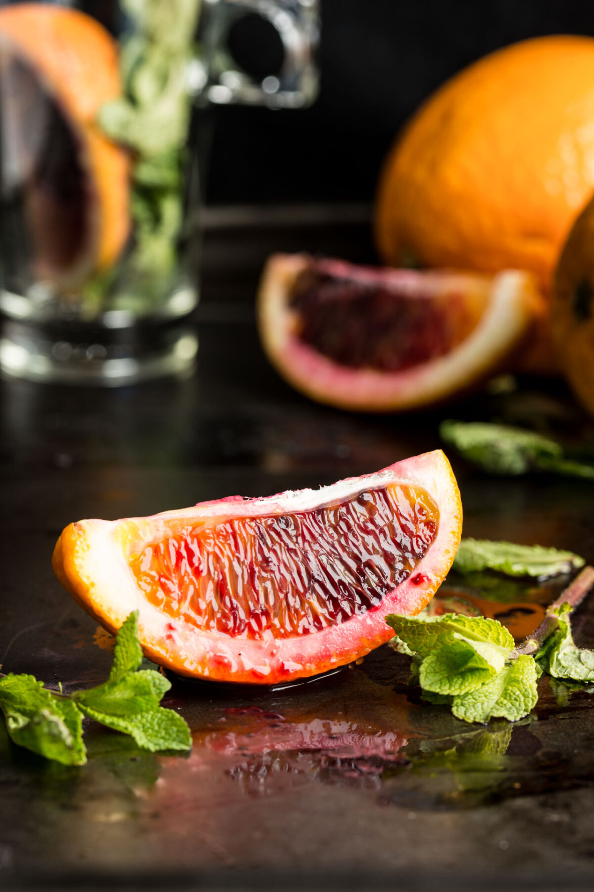 A slice of blood orange on a table surrounded by sprigs of fresh mint.