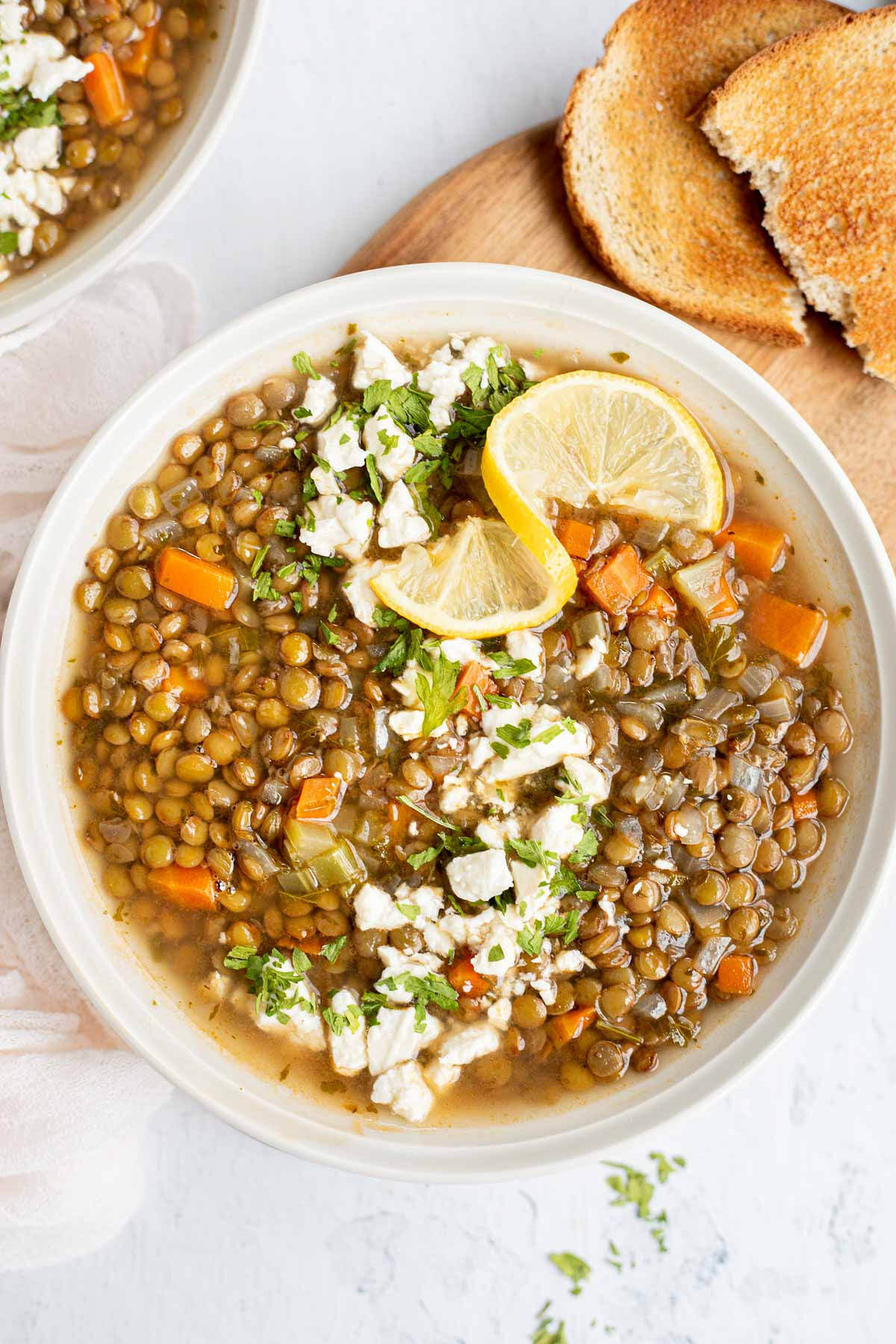 Vertical image of greek lentil soup with lemon and feta, with toast in the background.