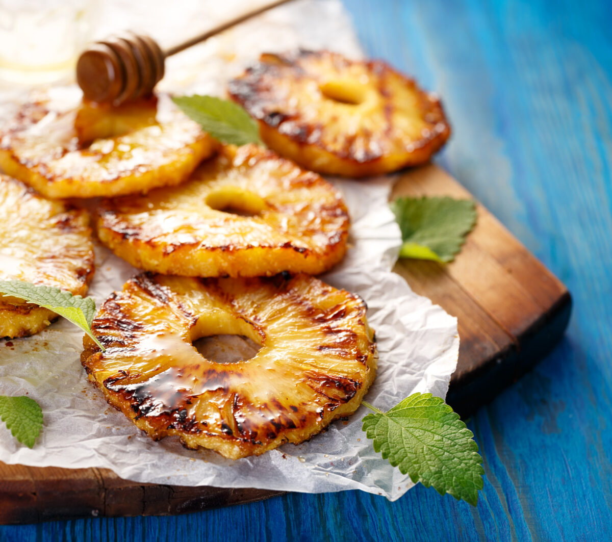 Grilled pineapple slices on a cutting board garnished with mint and drizzled honey.