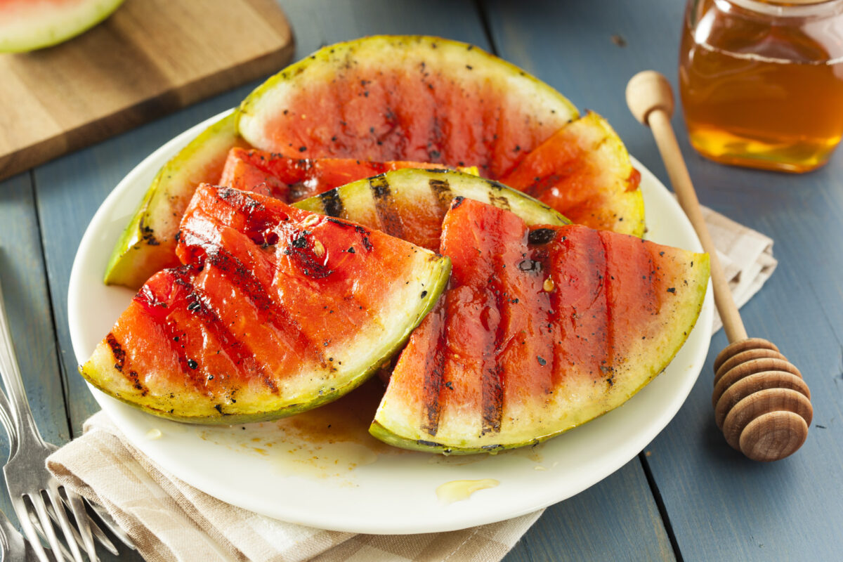 Grilled watermelon slices on a white plate with a jar of honey in the background.
