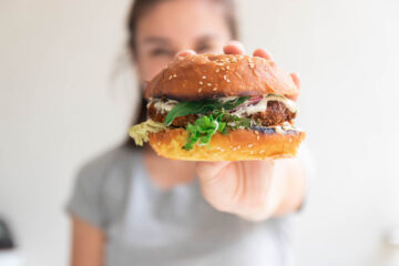 Woman holding a plat-based burger in her hand, out in front of her face.