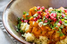 Sweet Potato and Chickpea Moroccan Style Stew in a tan glazed dish on top of a cloth napkin on a white speckled tabletop.
