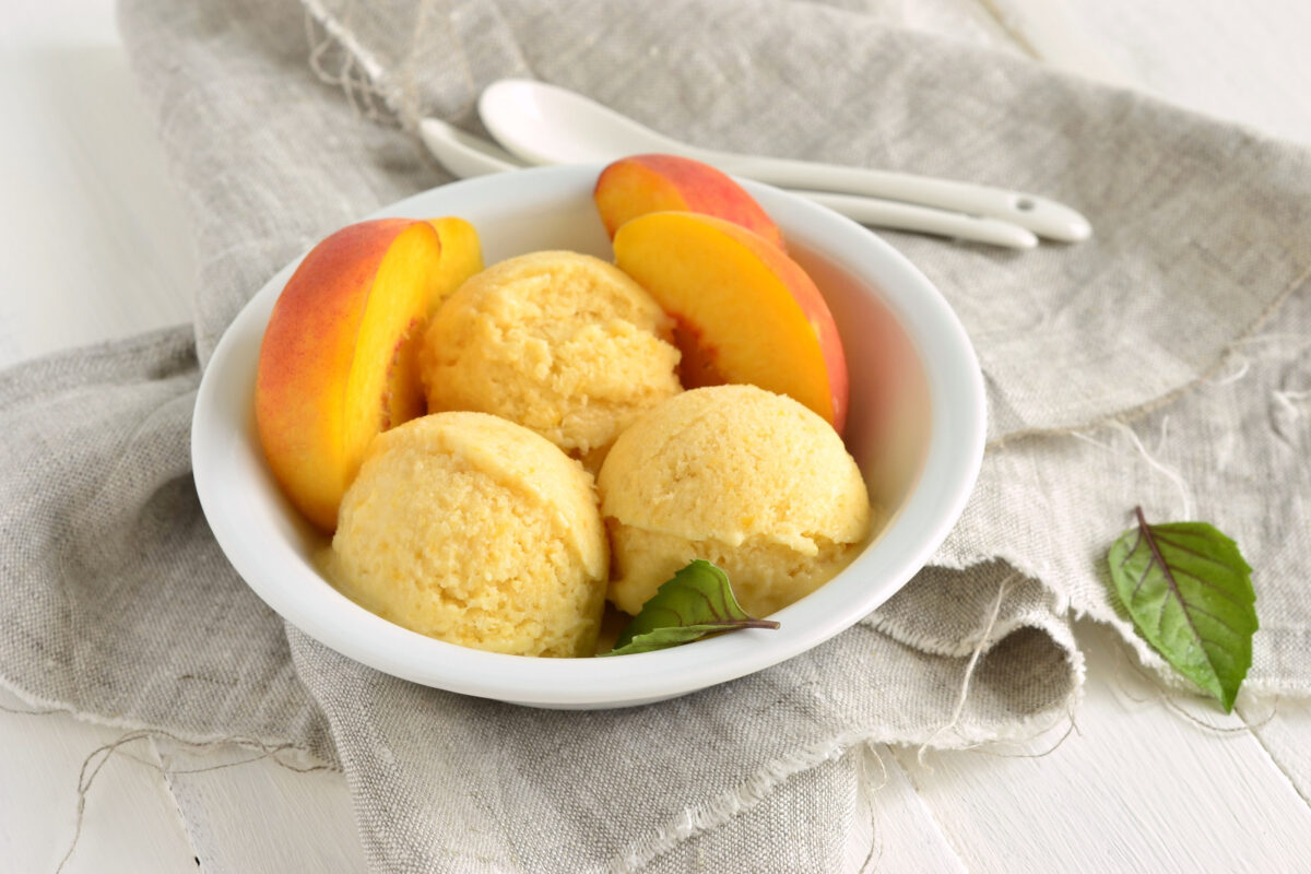 Peach ice cream with peach slices in a while bowl.