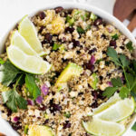 Quinoa salad with black beans and corn, garnished with cilantro and lime wedges.