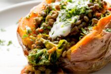 Cooked sweet potato filled with lentils, kale, and topped with yogurts on a white plate.