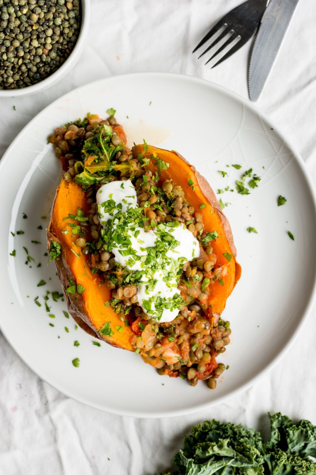 Sweet Potato stuffed with lentils, kale and sun dried tomatoes sprinkled with cilantro on a white plate and white background with fresh kale to the side.
