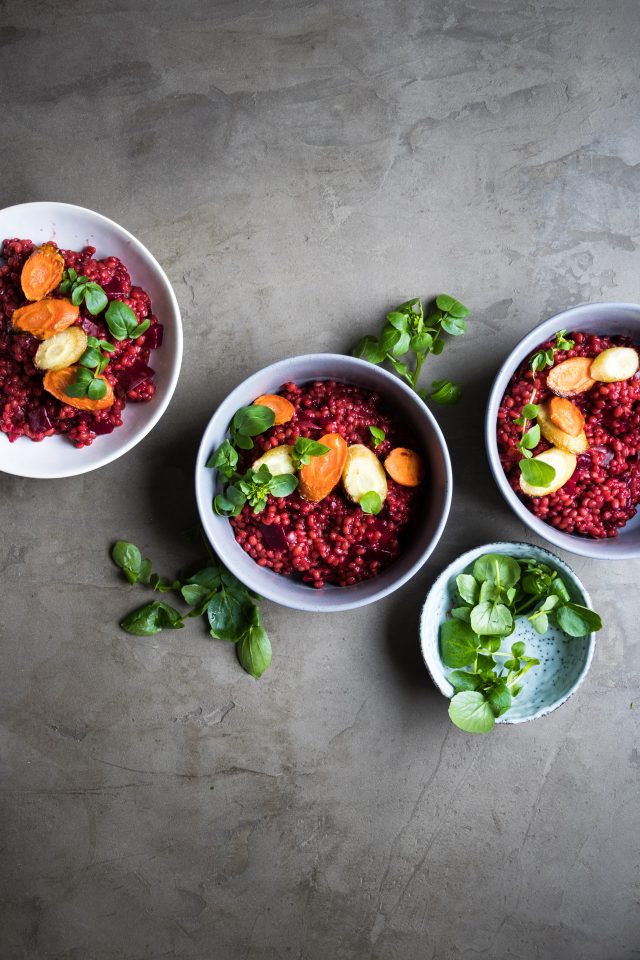 Top view of a red beet and barley risotto served with roasted carrots in white bowls.