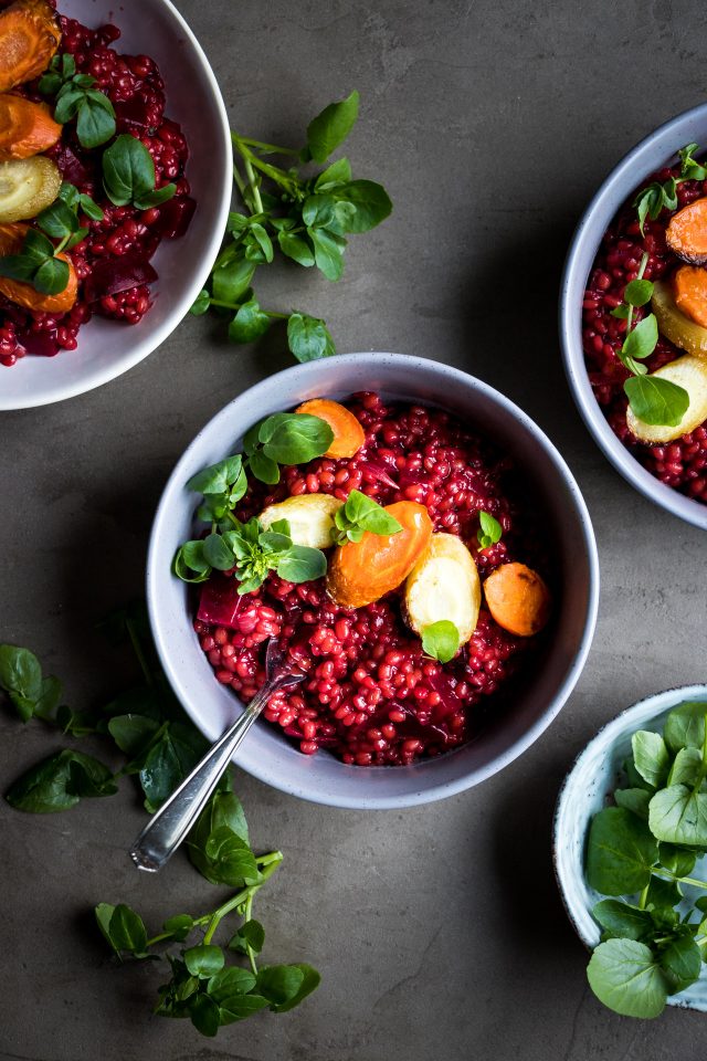 Top view of a red beet and barley risotto served with roasted carrots in white bowls.